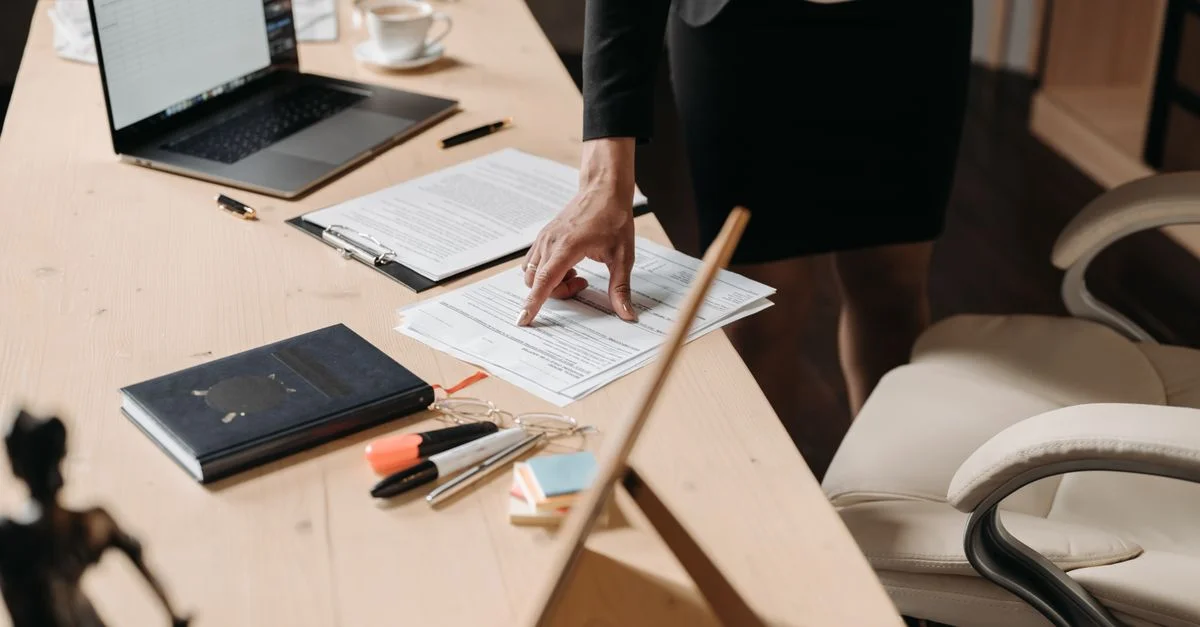 Femme d'affaires pointant des documents sur un bureau dans un cadre de bureau, mettant en évidence des données clés.